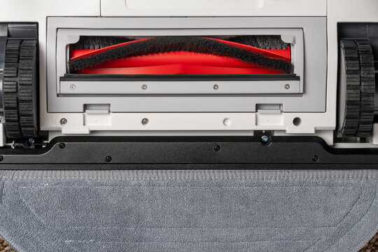 Closeup of underside of modern robot vacuum cleaner showing red main roller brush rubber wheels and grey microfiber mopping cloth pad for smart home cleaning technology