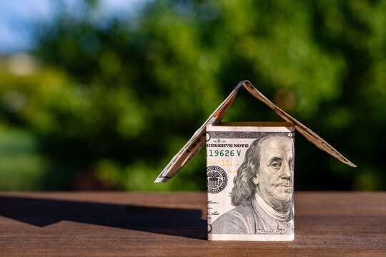 House made of US dollar bills on green natural background, closeup. Model small house built from one hundred dollar banknotes for real estate investment mortgage loan and financial banking concepts