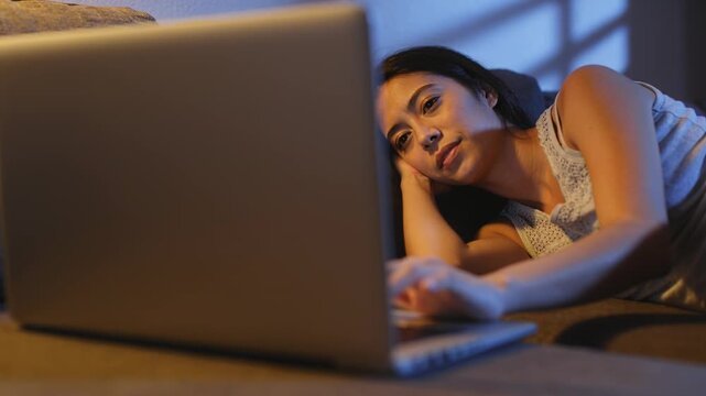 Asian woman in tank top lifting silver laptop on gray couch with hand resting, checking screen