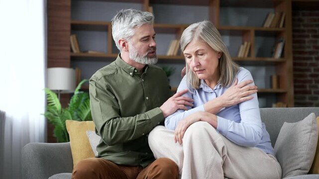 Close up of senior husband comforting his upset wife at home with caring words and emotional support. Retired couple sharing a difficult moment as the man gently reassures and encourages his partner.