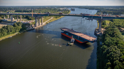 Aerial view of towing steel bridge deck section on pontoon barge for Rader High Bridge reconstruction. Transportation of massive steel segment on pontoon barge with a tugboat on the Kiel Canal. © snapshotfreddy