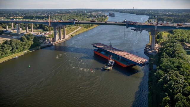 Aerial view of towing steel bridge deck section on pontoon barge for Rader High Bridge reconstruction. Transportation of massive steel segment on pontoon barge with a tugboat on the Kiel Canal.