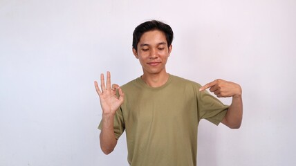 Fototapeta premium Asian young man smiling gestures pointing and looking at the middle side of the copy space and hands okay yes