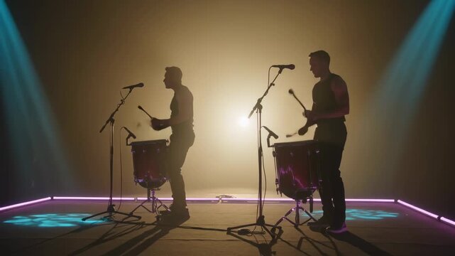 Playing two drummers after warm backlight cue on stage with timpani and mics, wearing dark clothing