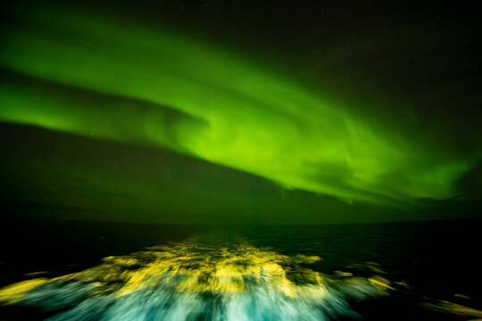 Ships wake shines under northern lights in the Denmark Strait at night