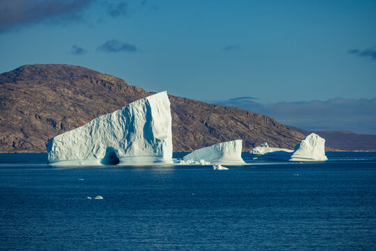 Towering icebergs drift across deep blue seas near Bjorneoer in the Arctic light under clear skies
