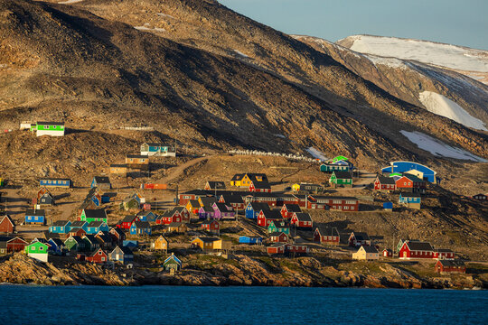 Colorful homes of Ittoqqortoormiit glow in evening light on Greenland's east coast by icy waters