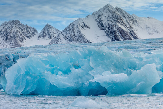 Glacier ice shards rise from the sea before snowy mountains at Alpefjord in Greenland's Arctic region