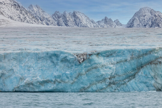 Glacier face towers above Arctic waters in Alpefjord with peaks in the distance