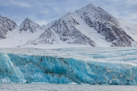 Glacier meets sea with blue hues under white mountain peaks in Alpefjord, Greenland