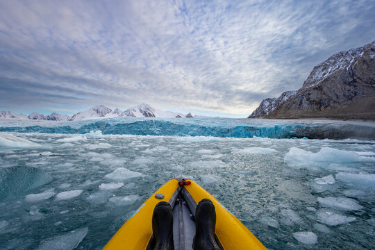 Kayaking among ice in Alpefjord with glaciers and mountains visible under a cloudy sky