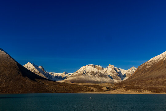 Bright snow-covered peaks rise above a calm bay with steep slopes under a blue Arctic sky near Blomsterbugten in Greenland