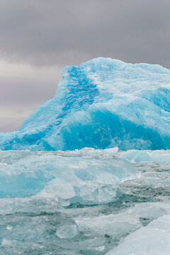 Towering blue iceberg rises above drifting sea ice in Arctic waters under grey skies