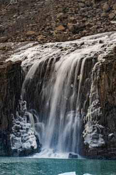 Cold Arctic waterfall streams over stone into turquoise water below