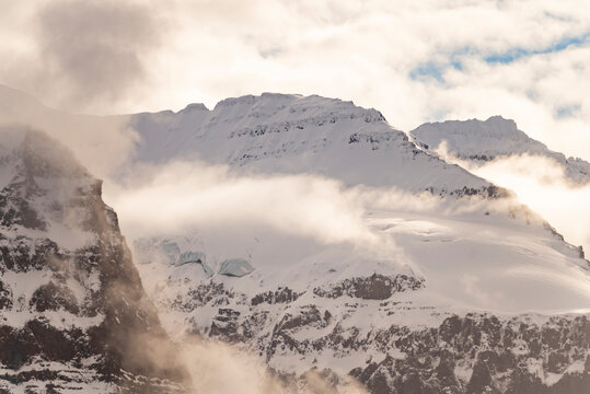 Close details of icy ridges and mist revealing textures of snow and rock in high peaks near Borgvig in Greenland