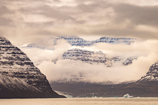 Mountains fade into clouds while snow-covered slopes appear through mist in Borgvig, Greenland