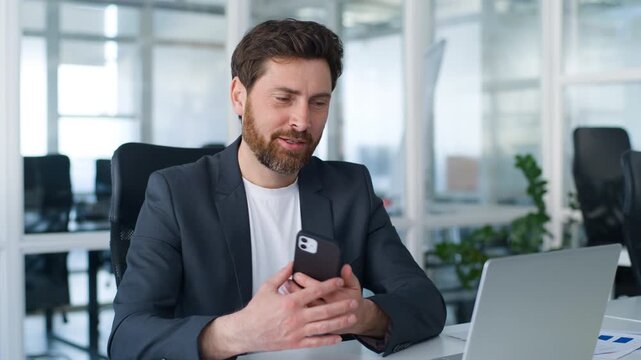 Pensive Caucasian middle-aged business man thinking calling mobile phone talking call at office table with laptop smiling mature businessman male employer think talk smartphone smile agent communicate
