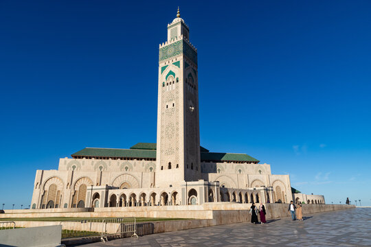 Visitors walk near Hassan II Mosque in Casablanca, Morocco on a clear sunny day with blue skies