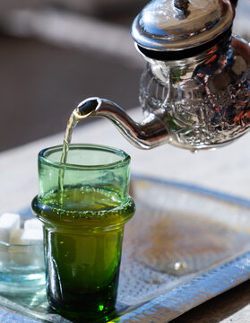 Traditional mint tea served in a silver teapot with sugar cubes on a metal tray in a Moroccan setting