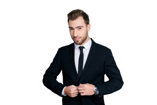 Portrait of handsome seductive tempting cunning smiling man wearing dark formal jacket with dark narrow tie, he is fastening the button on the clothing, isolated on gray background