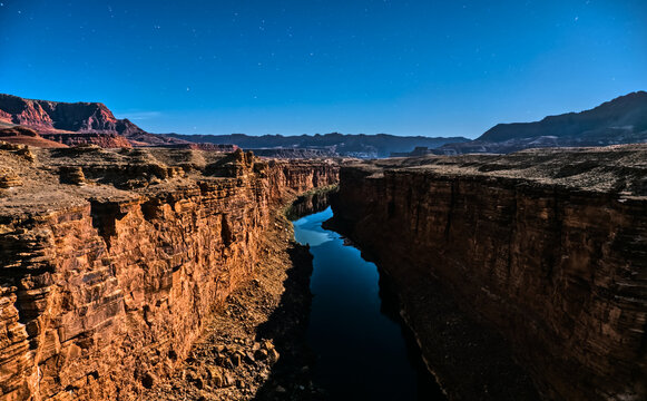 Moonlight casts soft light on the Colorado River flowing through Marble Canyon in Arizona at night under a starry sky