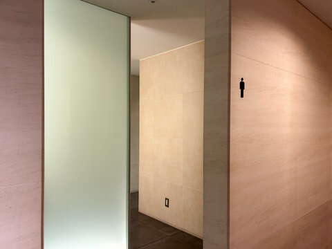 モダン男性公共トイレ入口、石目パネルと薄緑の曇りガラス間仕切りを使用した施設内装デザイン