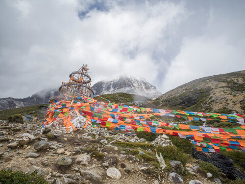 Colorful Tibetan prayer flags wave above a stone cairn in the mountains of Sichuan during a cloudy day