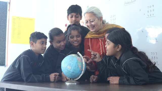 Senior indian teacher explaining geography concepts, pointing at globe with children as they engage learning activity during a school lesson, Education india.