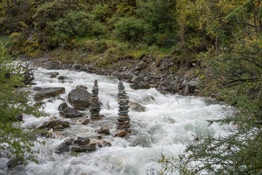 Fast mountain river with stone cairns along the bank in Yading National Park, Sichuan, China