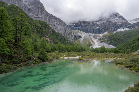 Exploring Pearl Lake in Yading National Park with forested slopes and rocky mountains under clouds in Sichuan, China