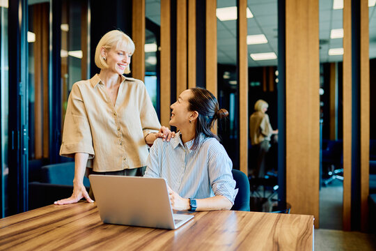 Two diverse businesswomen discussing strategy and working together on a laptop in a contemporary workplace environment, fostering support