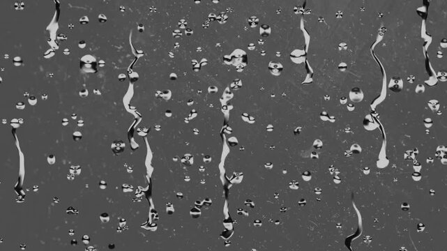 Raindrops adhere to a transparent glass surface creating a textured pattern with streaks of water.