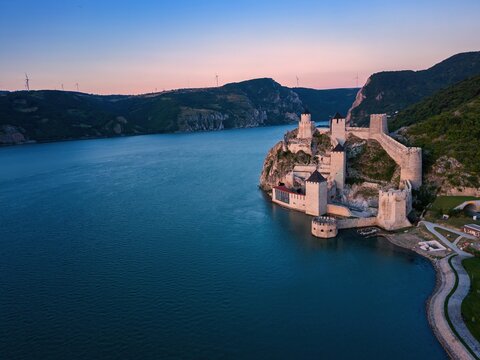 Drone view shows Golubac fortress by Danube river at sunset in Serbia, highlighting the structure's presence in nature's landscape