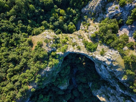Drone view showing Vratna caves natural arch and entrance surrounded by trees in Serbia