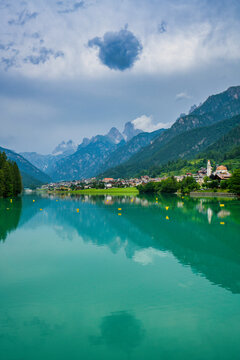 Mountains and village reflect on emerald waters of Lake Auronzo in Italy during a cloudy day
