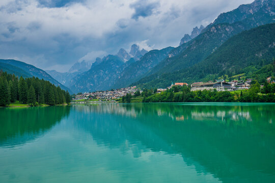 Mountains and village reflect on emerald waters at Lake Auronzo in Italy during daytime