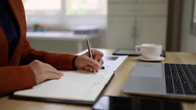 Businesswoman writing meeting notes in notebook while sitting at her office desk