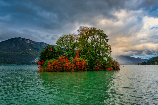 Colorful autumn foliage on an island in Lake Annecy with trees and changing skies in France
