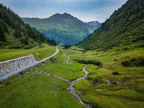 Winding road and flowing stream through green valley in the Austrian Alps near Sankt Anton am Arlberg in Tyrol