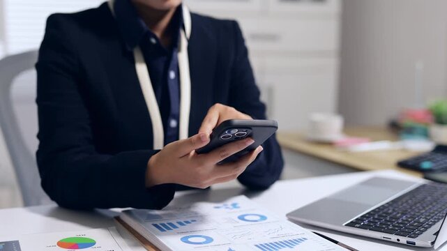 Businesswoman scrolling on smartphone and analyzing financial data in the office