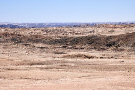 Trockene H&uuml;gellandschaft mit dunklem Felsr&uuml;cken und hellen Ebenen bei Swakopmund in Namibia.