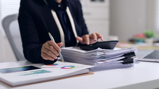 Businesswoman analyzing charts and using calculator for financial auditing