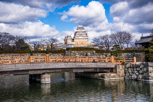 Wooden bridge and moat leading to Himeji Castle with reflection of architecture under blue sky in Japan