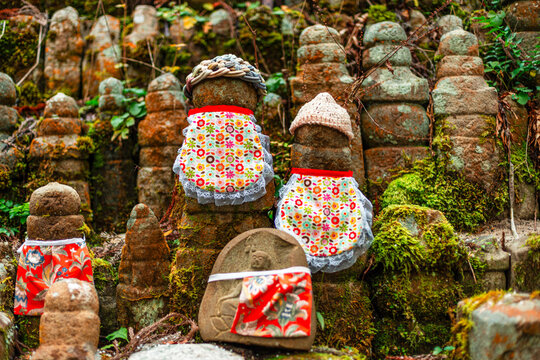 Stone statues covered in colorful cloths and moss at Okunoin Cemetery with greenery surrounding them in Japan