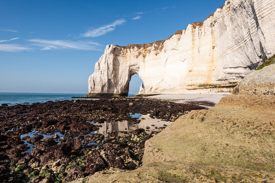 View of Manneporte arch among cliffs in Normandy with rocks by the shore and blue sky above from the Alabaster Coast trail