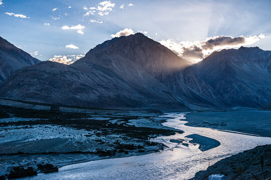 Sunrise light spreads over the braided channels of Shyok River in Nubra Valley, surrounded by mountains in Ladakh, India