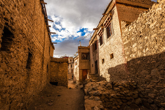 Explore narrow alleyway through historic mud-brick houses in old Leh, India under warm sunlight