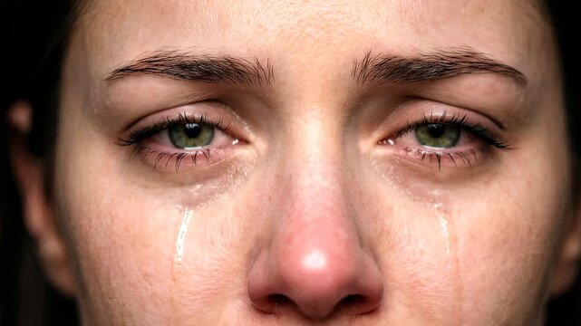 Crying woman with green eyes and tears streaming down cheeks. Extreme close-up shot with tilting camera movement.