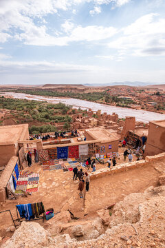 Handmade rugs are sold by local vendors on a rooftop market in a scenic area with distant river views in Morocco
