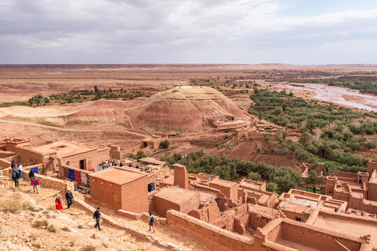 Visitors walk through the mudbrick village of At Benhaddou under cloudy skies near the Ounila River in Morocco